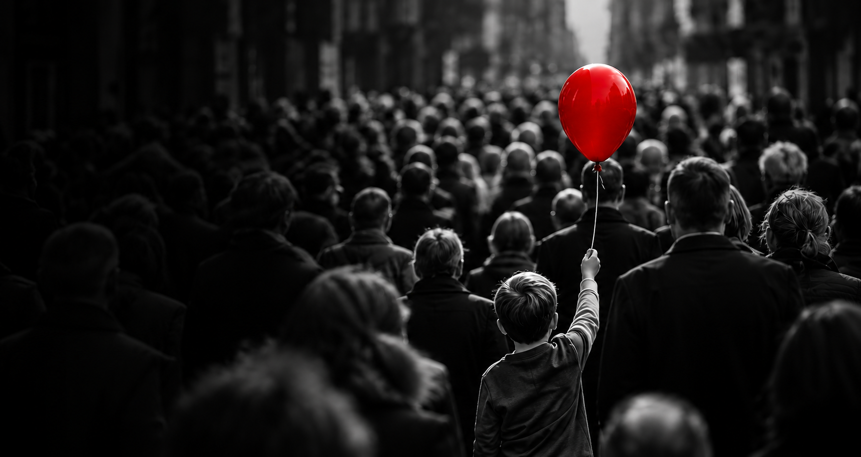 A boy raises a red balloon above a monochrome crowd